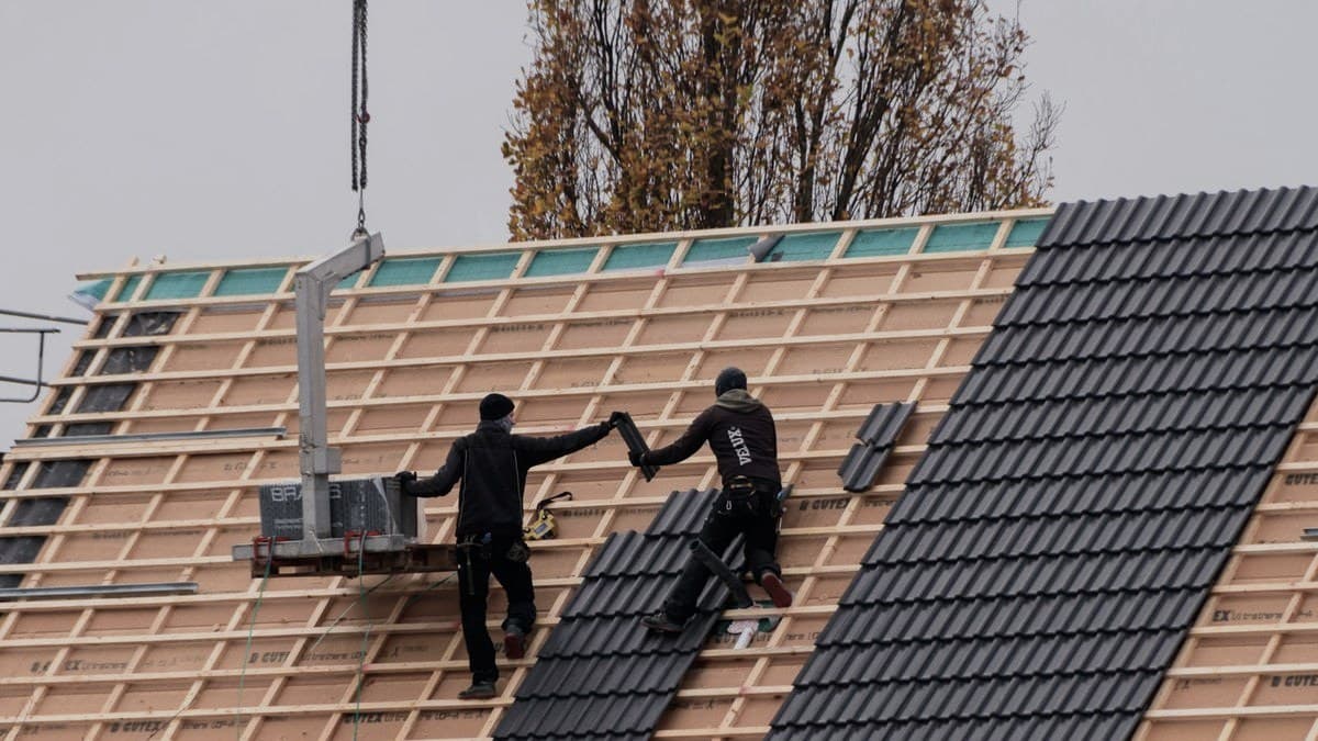 Two roofers installing tiles on a house roof